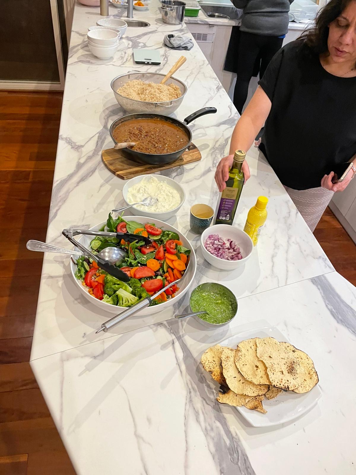 Nutritious vegetarian meals being prepared at the Mystique Moksha Samatvam Retreat; a spread of fresh garden salads, traditional dhal, and papadums on a white marble kitchen island, highlighting the healthy retreat catering at Yanada, St Albans.